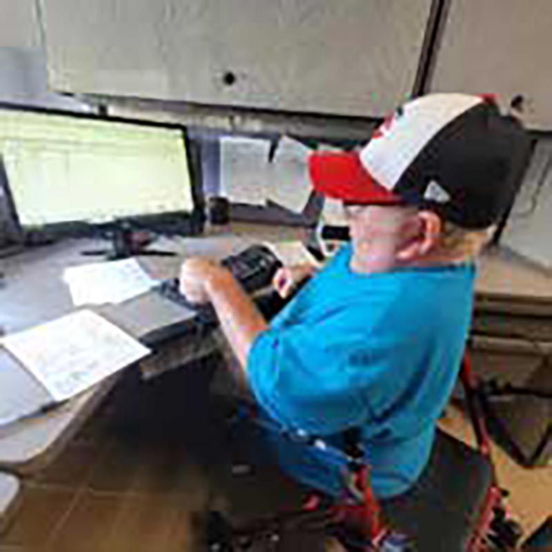Young man in baseball cap and using a wheelchair works at a bank of computer monitors