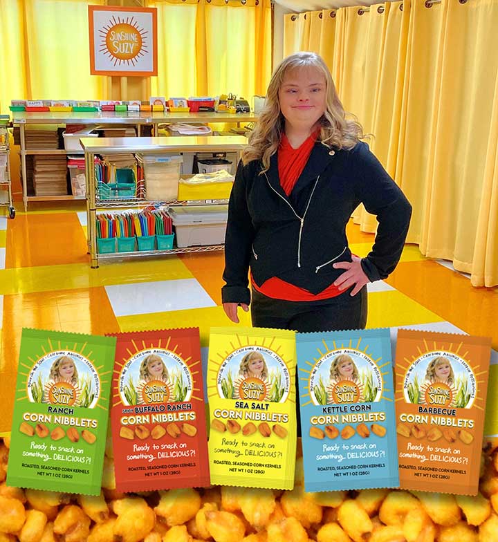 Suzy, a woman in her 20s with blond hair, red shirt, black pullover and black pants, stands in front of products she sells through her microbusiness called Sunshine Suzy's Corn Nibblets