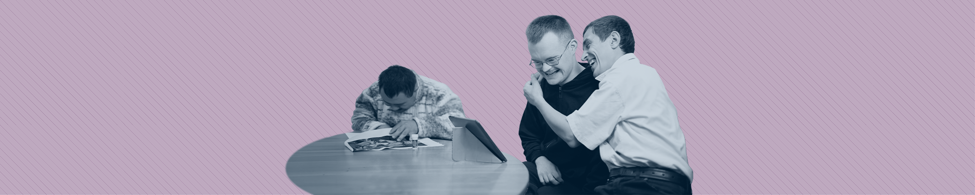 Two men with disabilities laughing and embracing while sitting at a table.