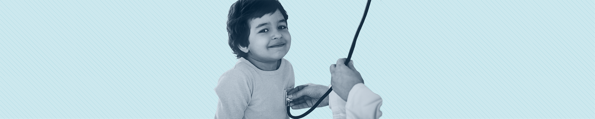 A toddler smiles into the camera while a doctor uses a stethoscope to listen to him breathe.