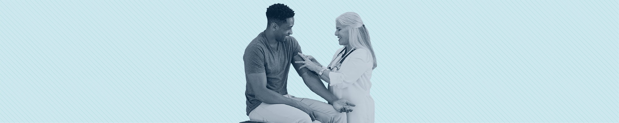 A doctor takes a young man's blood pressure while they both laugh.