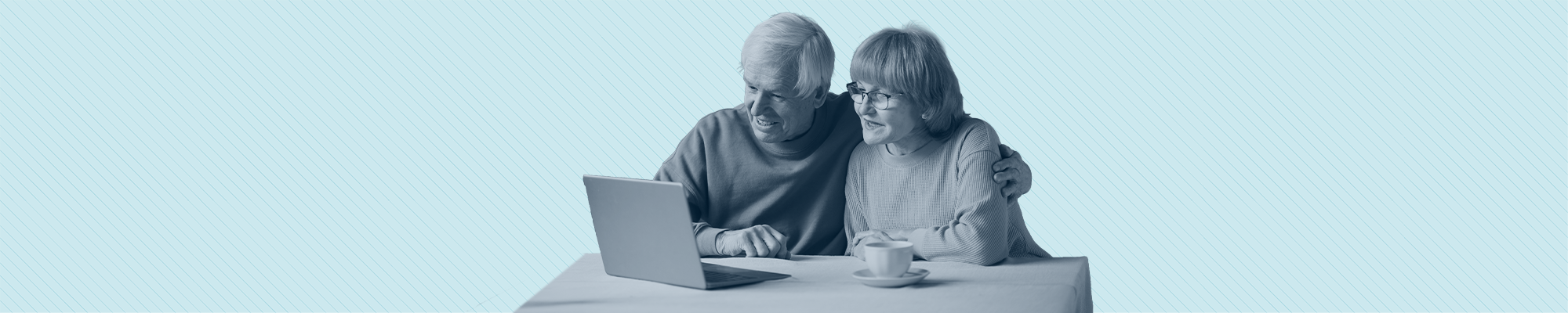 An elderly couple look at a laptop while sitting at a table.