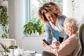 A woman assisting another woman who is sitting down by a table